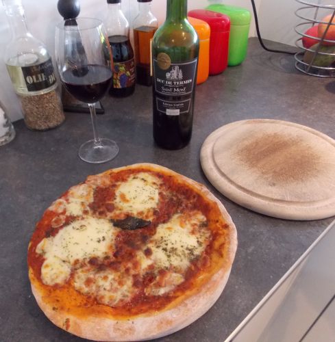 Foto van een zojuist gebakken pizza met hiernaast een fles Frans rode wijnt. Een 'Duc de termes' uit 2013.